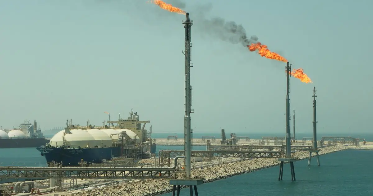 An LNG carrier berthed at the Ras Laffan terminal, with gas flares burning